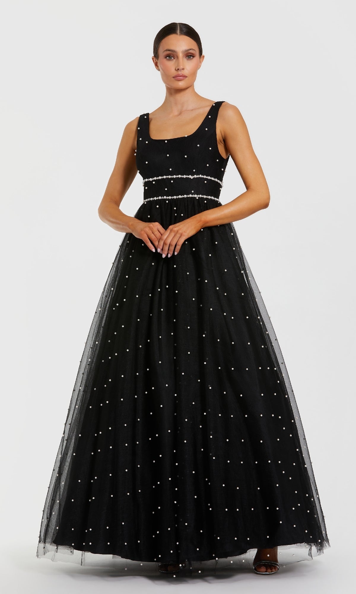 A woman wearing the Mac Duggal 56204 long formal dress—a sleeveless black ball gown with white polka dots and a tulle A-line skirt—stands against a plain white background.